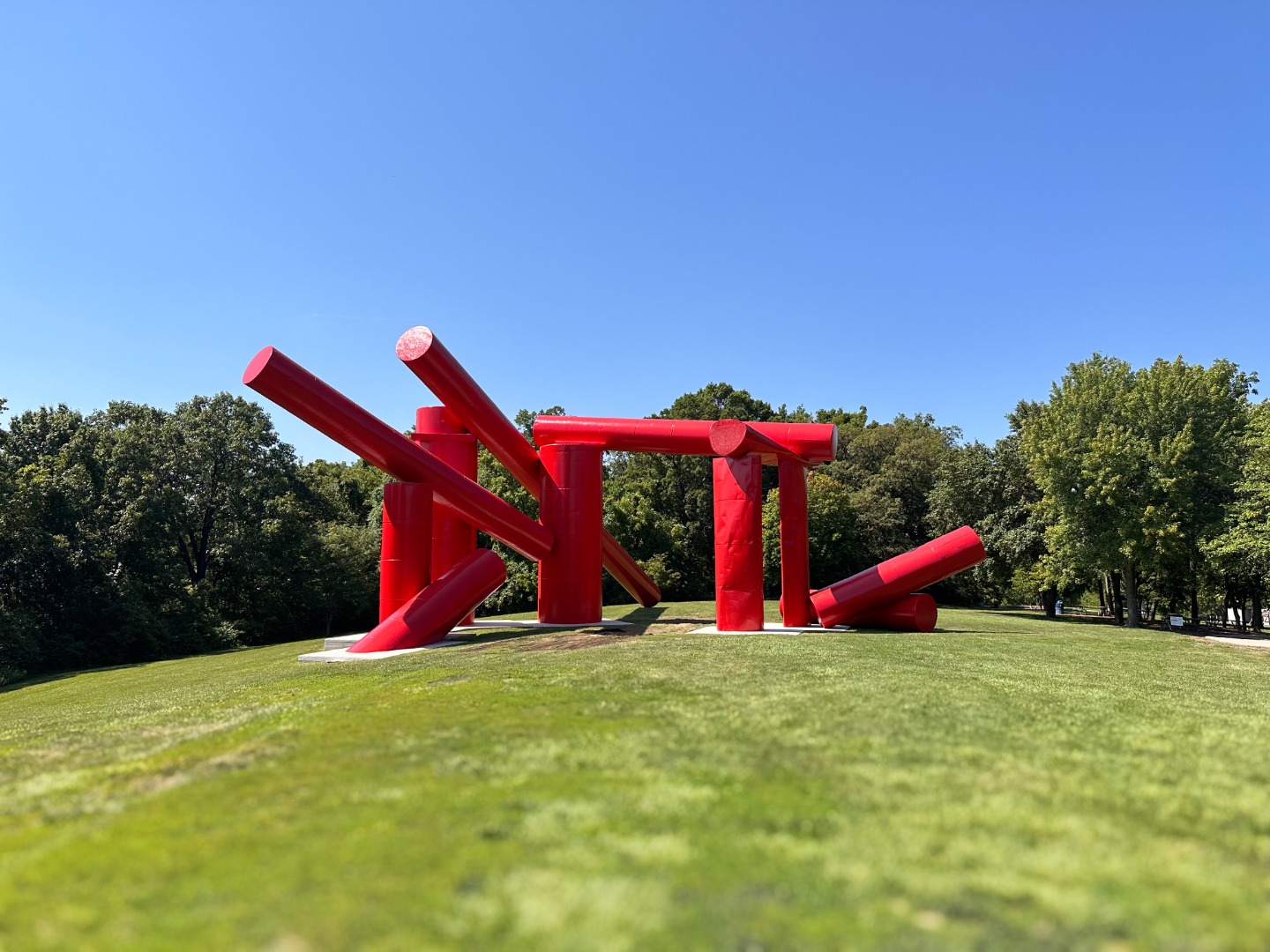 A bright red sculpture made of large steel tanks is on display in a park clearing. 